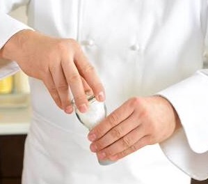 chef adding salt to a dish