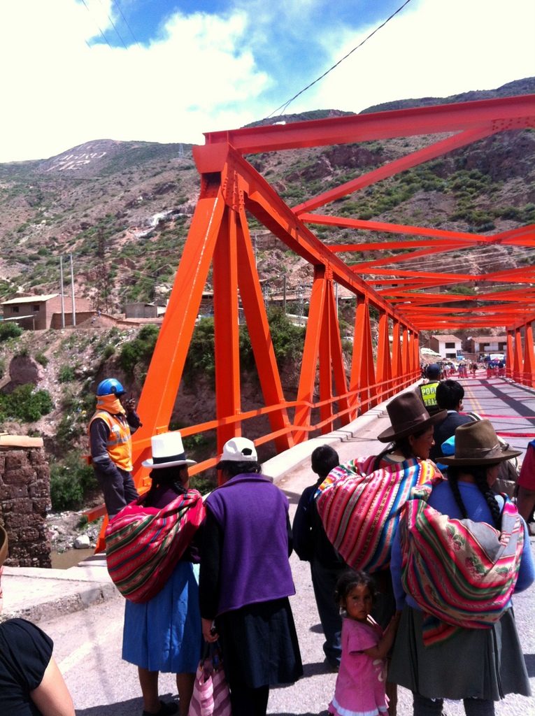 Women in traditional high mountain Peruvian dress halted at a structurally compromised bridge