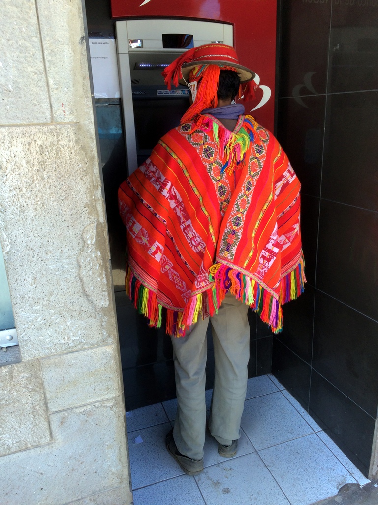 Man in traditional brightly colored hand woven pancho standing at an ATM