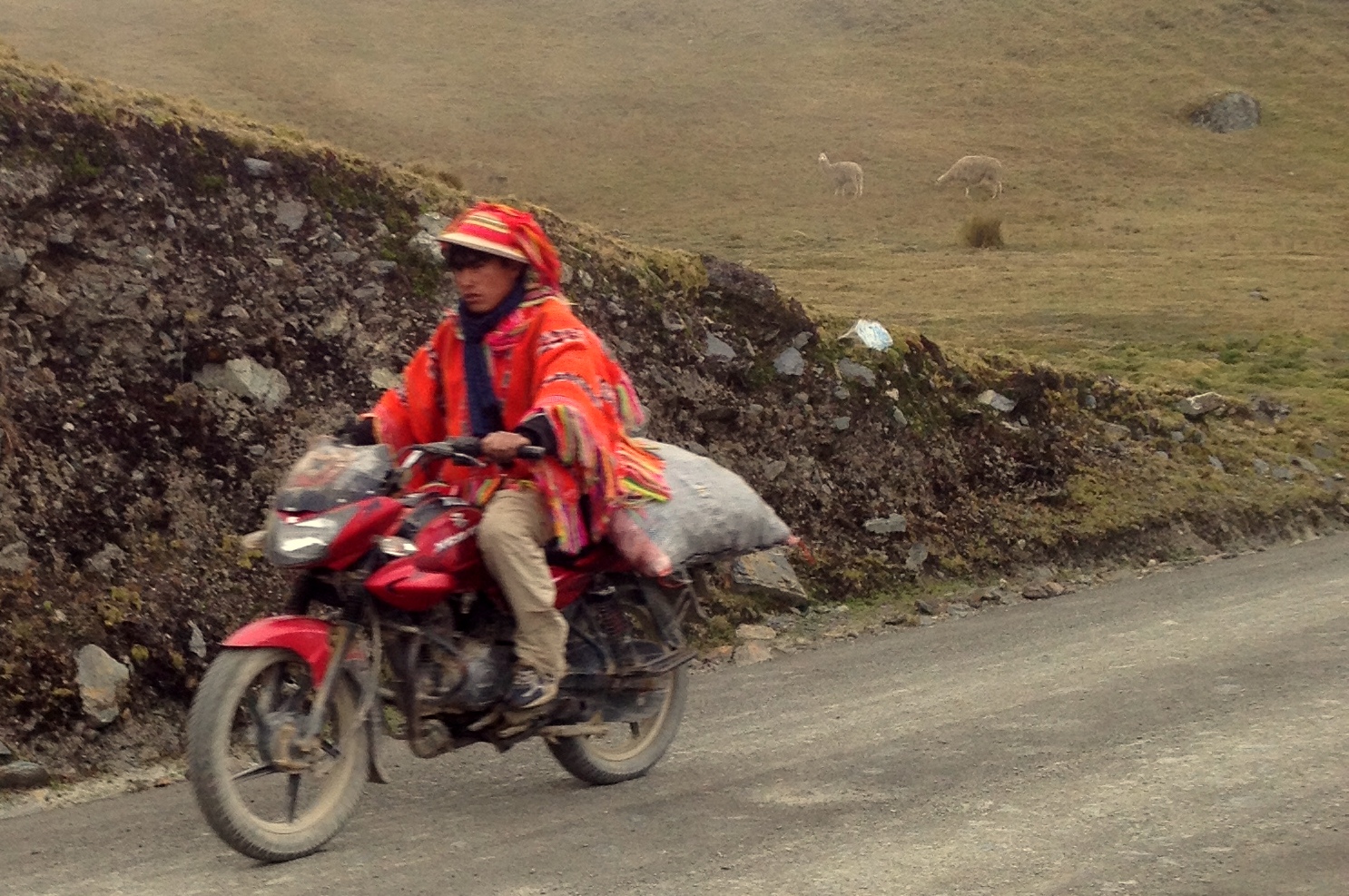 Young man in traditional handwoven brightly colored poncho riding a motorcycle.