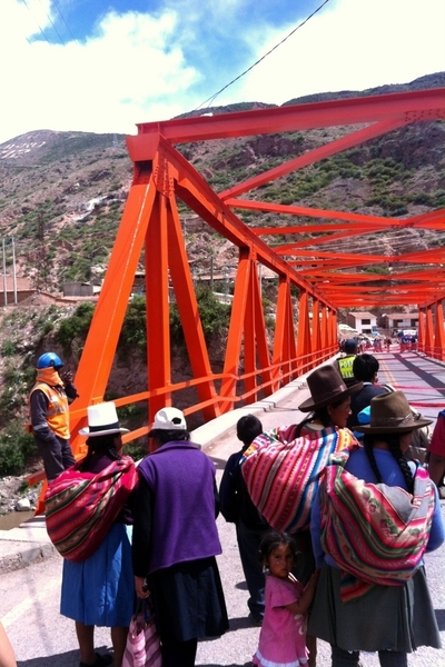 Women in traditional high mountain Peruvian dress halted at a structurally compromised bridge