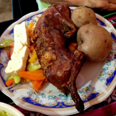 A small roasted cuy on the plate next to potatoes, Andean cheese, and vegetables