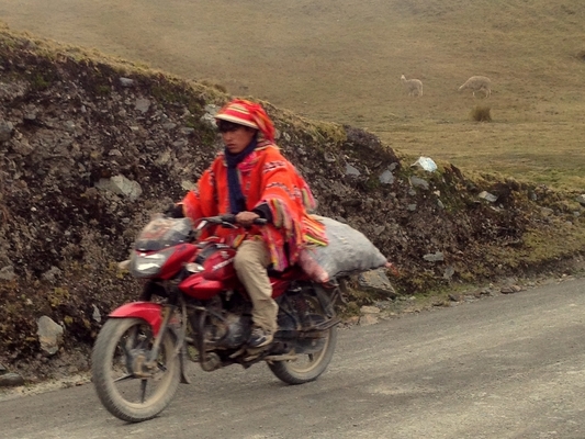 Young man in traditional handwoven brightly colored poncho riding a motorcycle.